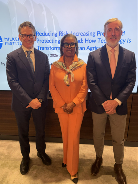 Three professionals in business attire posing together at a formal event, woman in orange suit between two men in dark suits